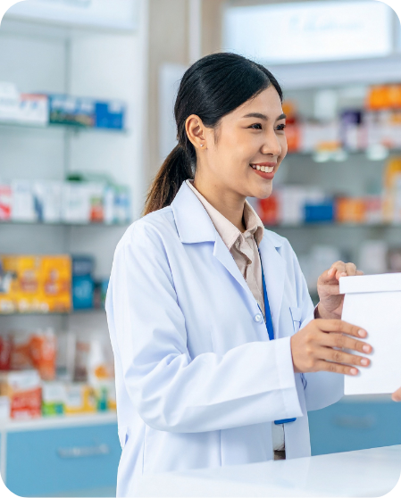 Pharmacist in a white lab coat handing a box to a customer at a pharmacy counter, smiling.